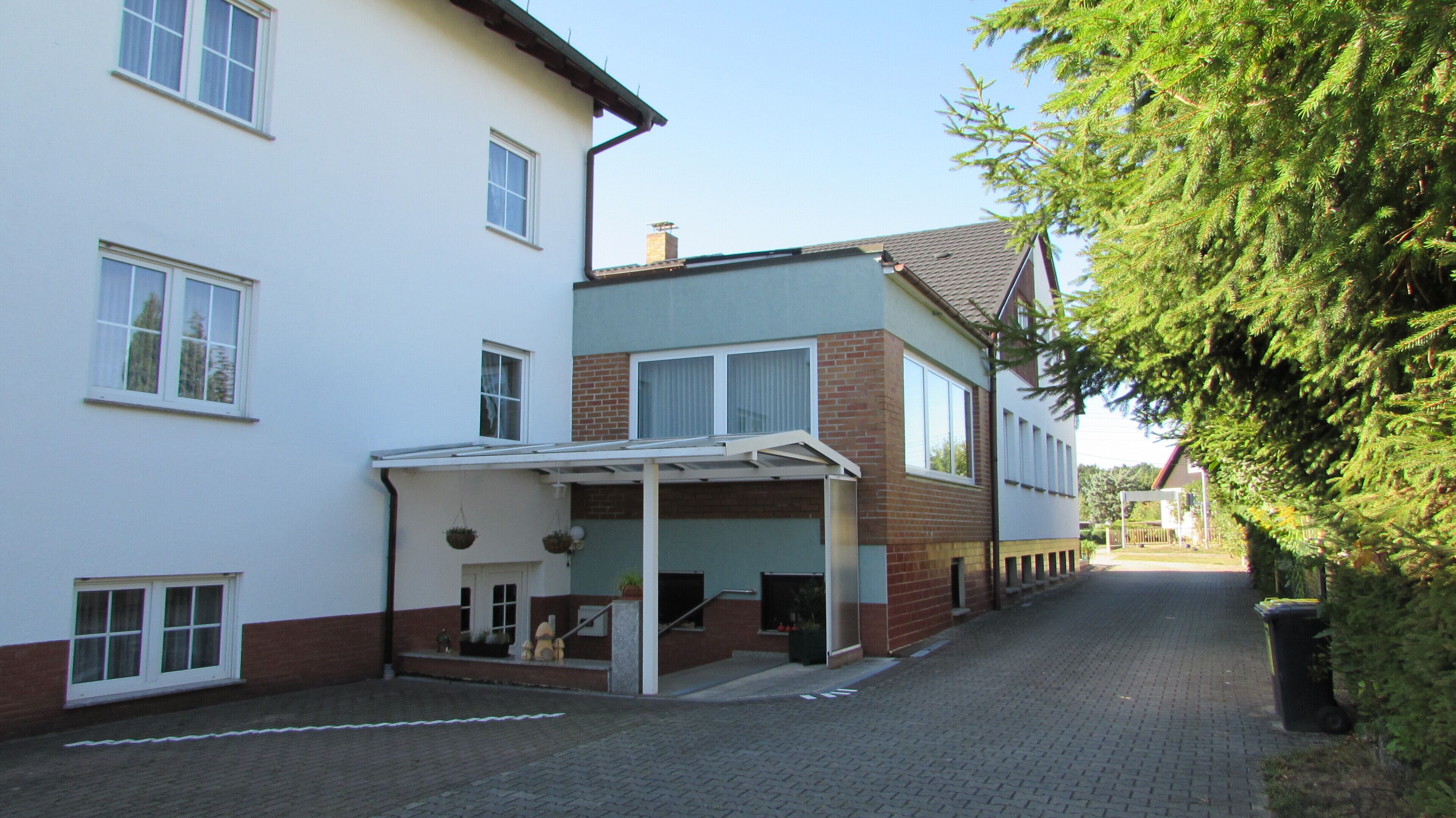 A two-story residential building with a covered porch, a brick section, and a clear sky.