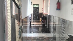 A hallway with a marble floor, a fire extinguisher mounted on the wall, and a motorcycle parked in the distance. - Hotel T Star (Meerut)
