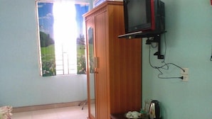 Une chambre avec une armoire en bois, un téléviseur fixé au mur, une petite table avec une bouilloire et une fenêtre donnant sur un paysage verdoyant.