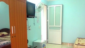 Une chambre à coucher avec un lit, une armoire en bois, une télévision, un ventilateur et une porte.