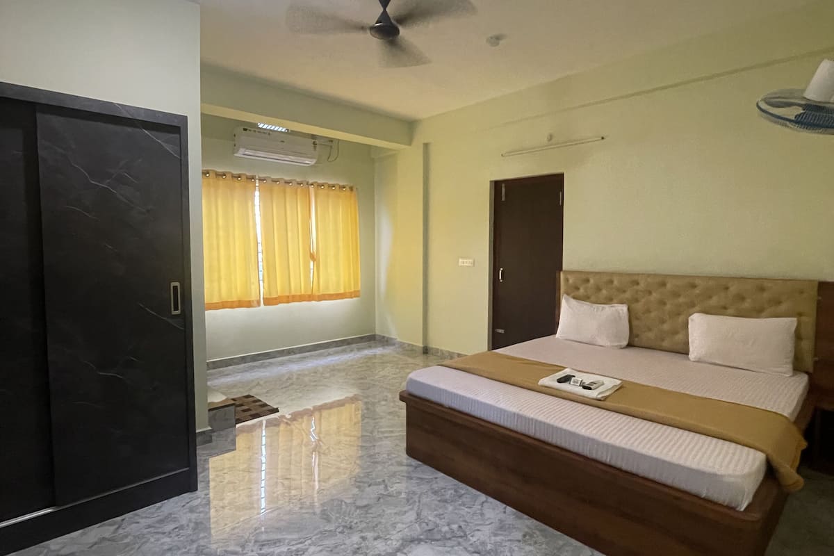 Une chambre à coucher comprenant un lit, un ventilateur de plafond, un appareil de climatisation et une porte.