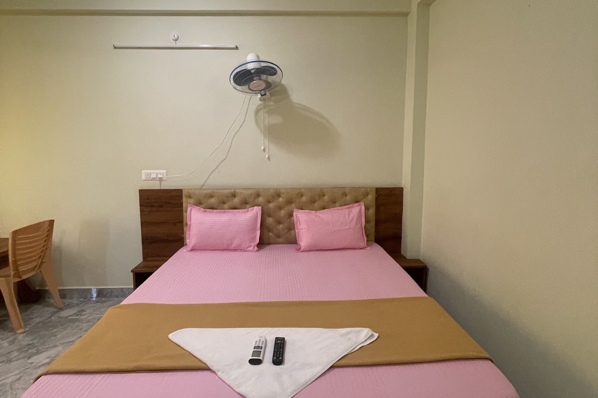 Une chambre à coucher comprenant un lit, une table de chevet, une chaise, un ventilateur de plafond et un luminaire fixé au mur.
