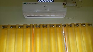 Una habitación con una cortina amarilla, un equipo de aire acondicionado blanco y una ventana con persianas horizontales.