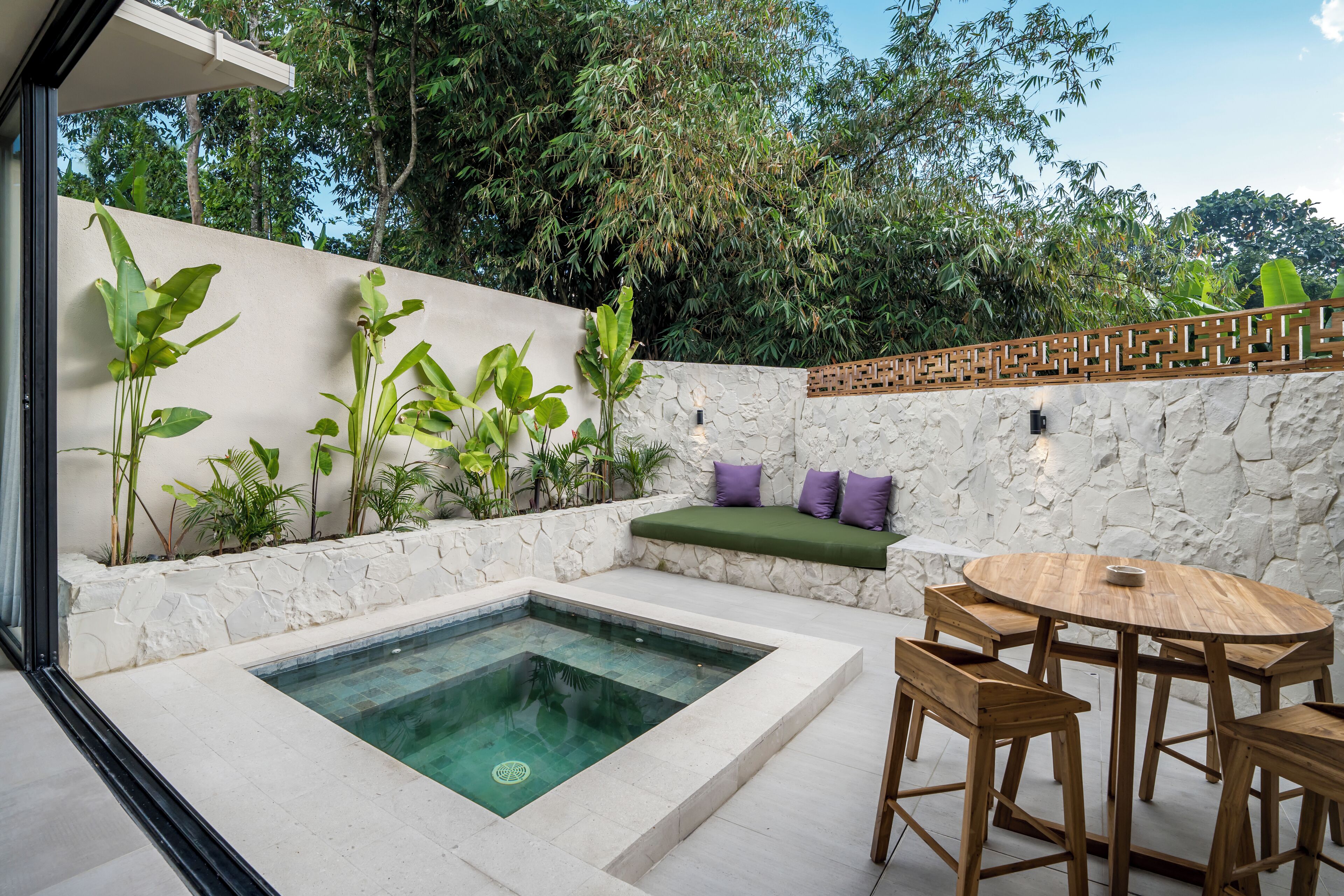A modern outdoor pool area with a stone wall, wooden seating, and a round table.