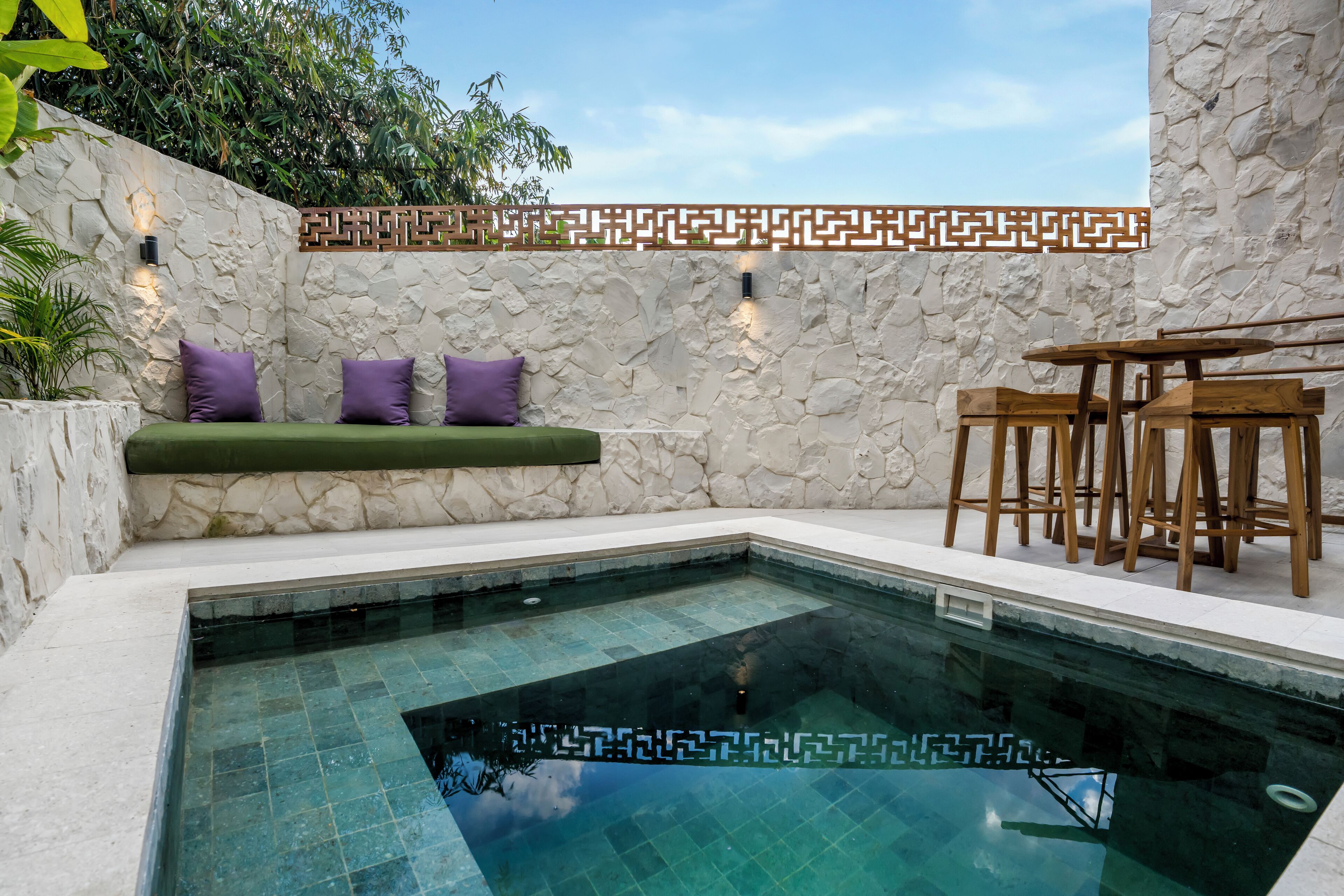 A pool area with stone walls, a bench with cushions, and wooden chairs.