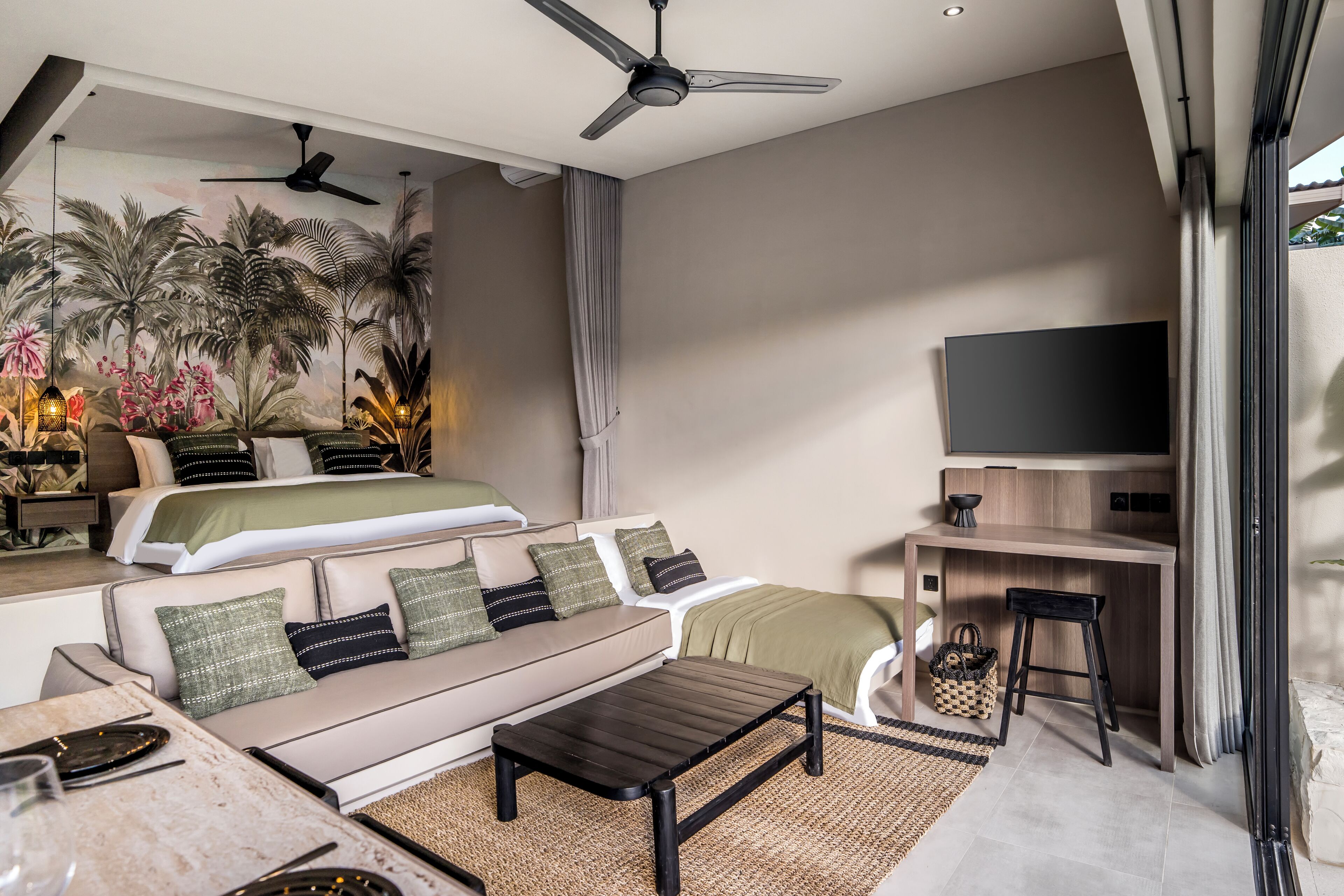 Una habitación de hotel moderna con cama, sofá, mesa de centro, televisor y ventilador de techo.