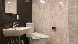 Ένα σύγχρονο μπάνιο με λευκό νιπτήρα, τουαλέτα και ντους. Οι τοίχοι είναι επενδυμένοι με συνδυασμό σκούρων και ανοιχτόχρωμων πλακιδίων και πάνω από τον νιπτήρα υπάρχει ένας καθρέφτης.