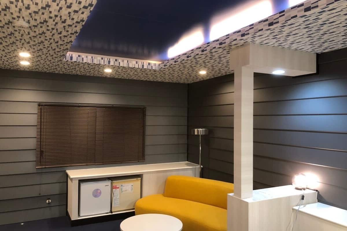 A modern room with a dark grey wall, a yellow sofa, a white table, and a cabinet with a small fridge.