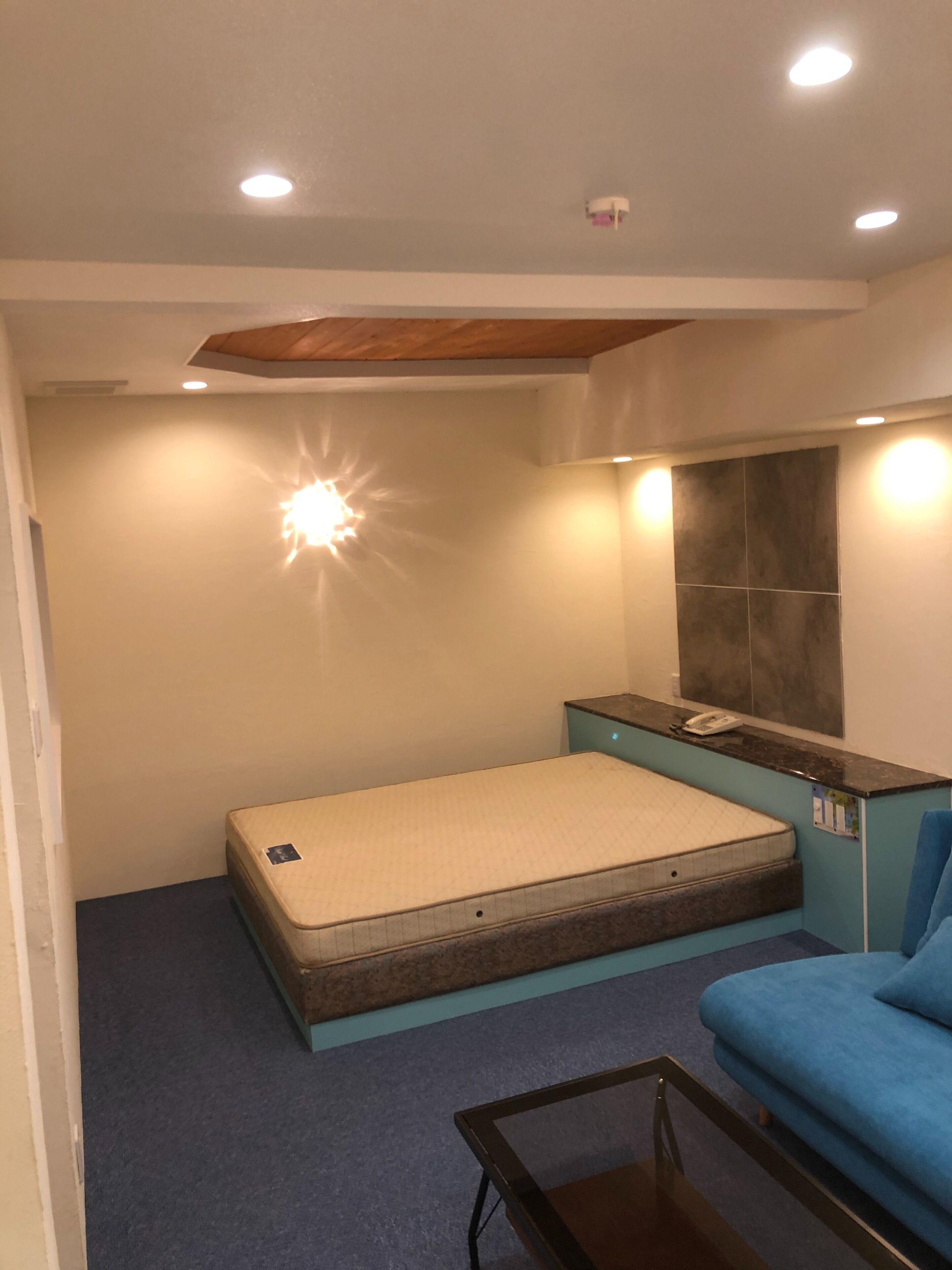 Una habitación pequeña con una cama, una mesita, un sofá azul y un teléfono instalado en la pared.