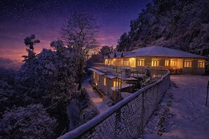A snow-covered landscape with a house featuring a balcony and a view of the night sky. - The HillCrest (Dehradun)
