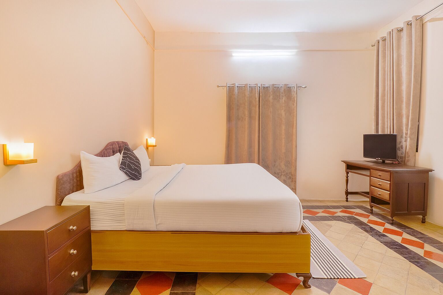 Une chambre d’hôtel comprenant un lit, une table de chevet, une lampe, une télévision et des rideaux.