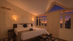 A bedroom with a bed, bedside tables, a nightstand, a window with a view of the sunset, and a checkered floor. - The HillCrest (Dehradun)