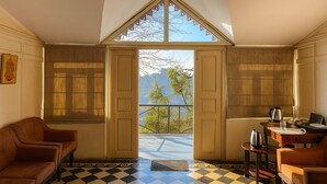 A room with a checkered floor, a brown leather sofa, a wooden cabinet, and a table with a kettle and a glass. - The HillCrest (Dehradun)