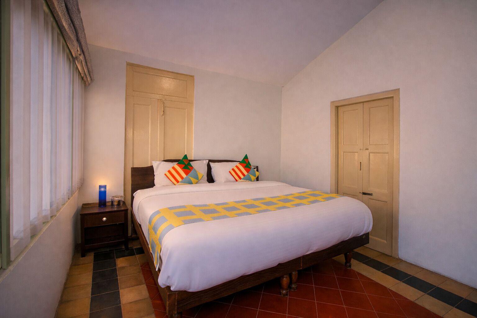A bedroom with a bed, nightstands, a window with curtains, and a door.