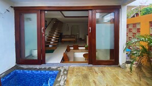 Una casa moderna con puerta de cristal que da a un área de estar con escalera, comedor y una piscina pequeña.