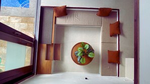 Una habitación con una cama, un adorno circular en la pared y una ventana con vistas a un cielo azul y un muro de piedra.