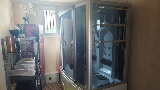 Una habitación compacta con sauna de cristal, un ventanal pequeño y un tapete amarillo en el suelo.