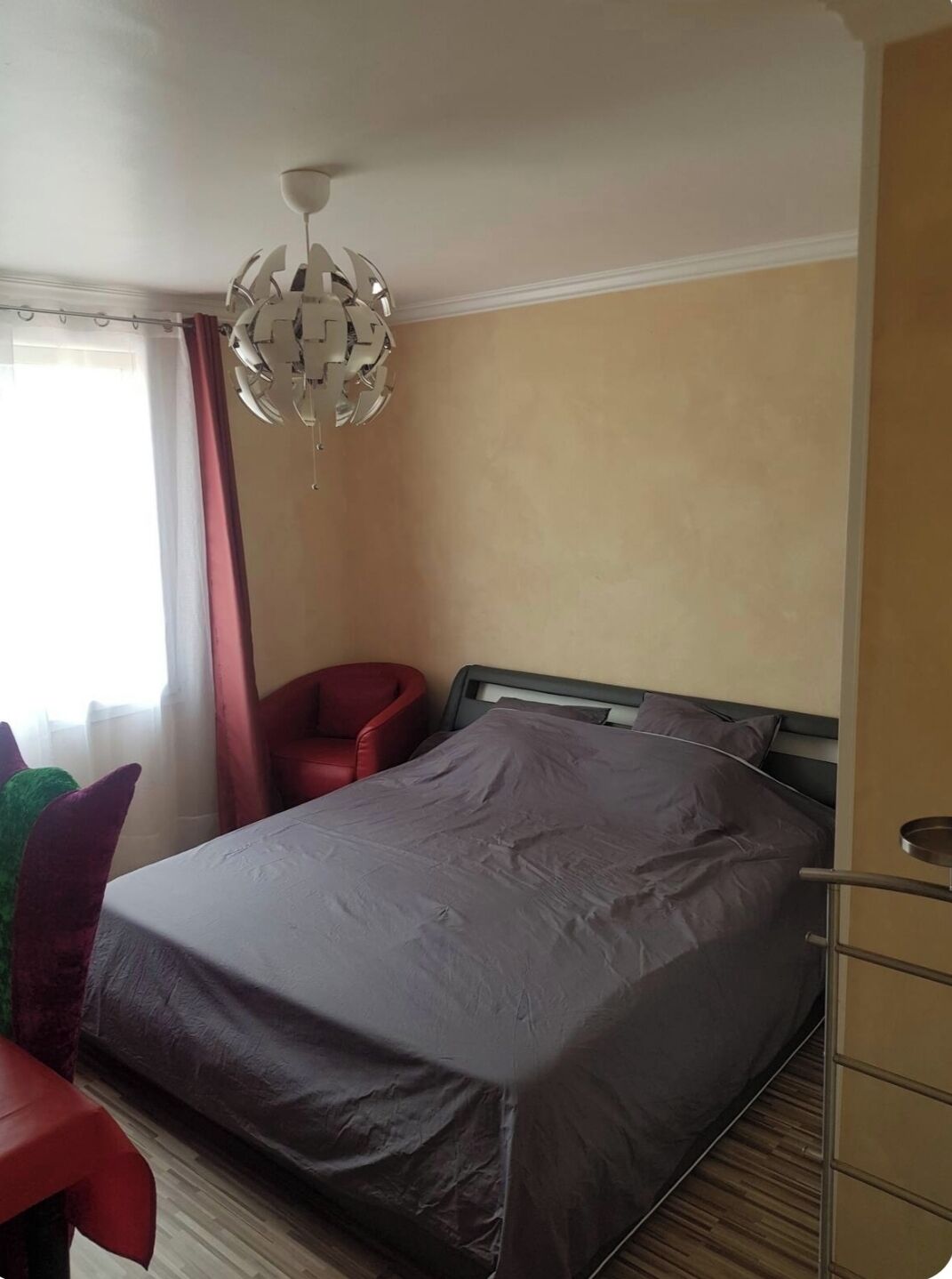 A hotel room with a bed, a red chair, a desk, and a chandelier.