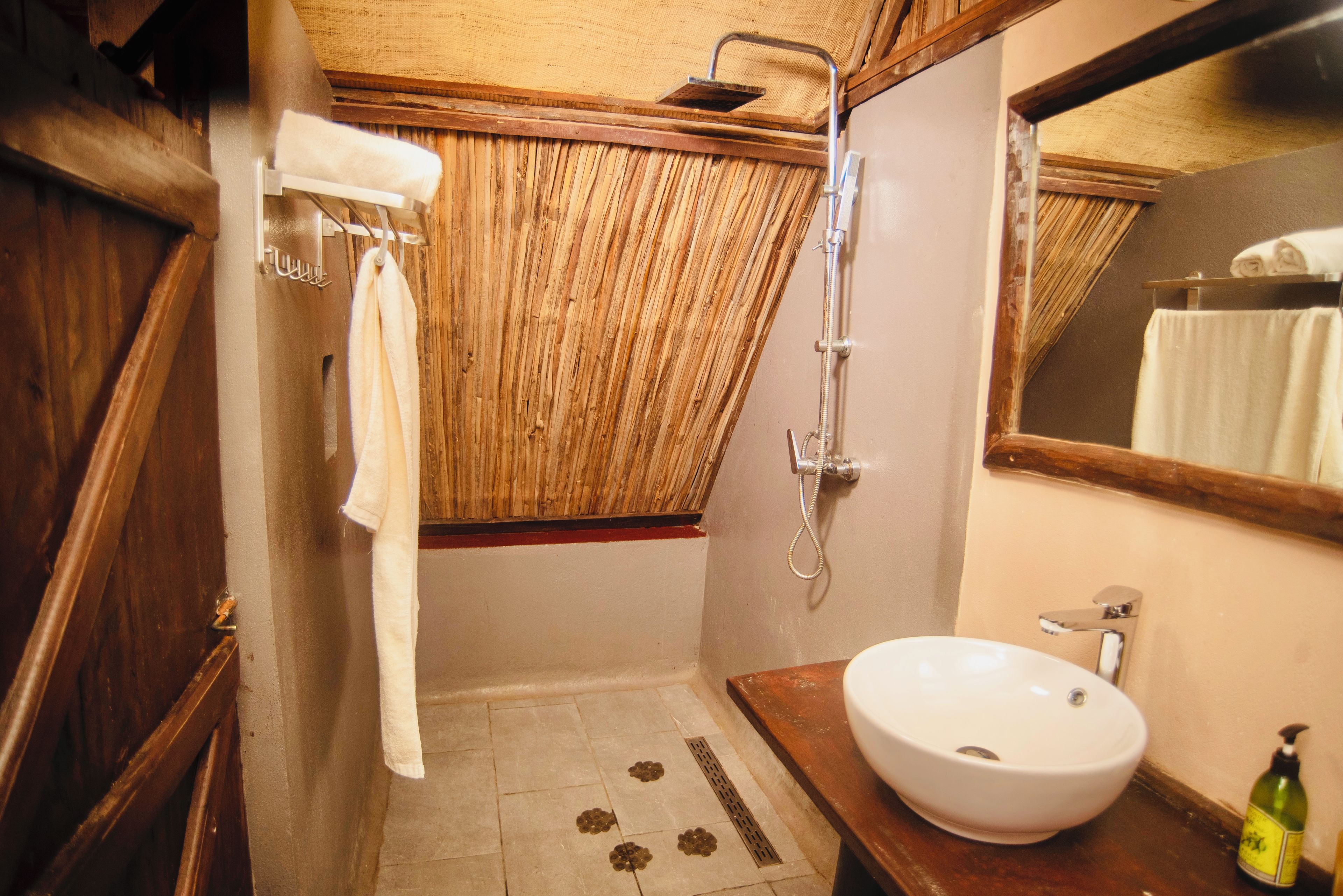 A compact bathroom with a wooden floor, a white sink, a mirror, and a shower.