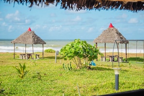 A beach with two thatched-roof structures, a grassy area, and the ocean in the background.