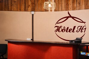 Un mostrador de recepción de hotel con un logotipo, una lámpara colgante y un cartel con un mensaje.