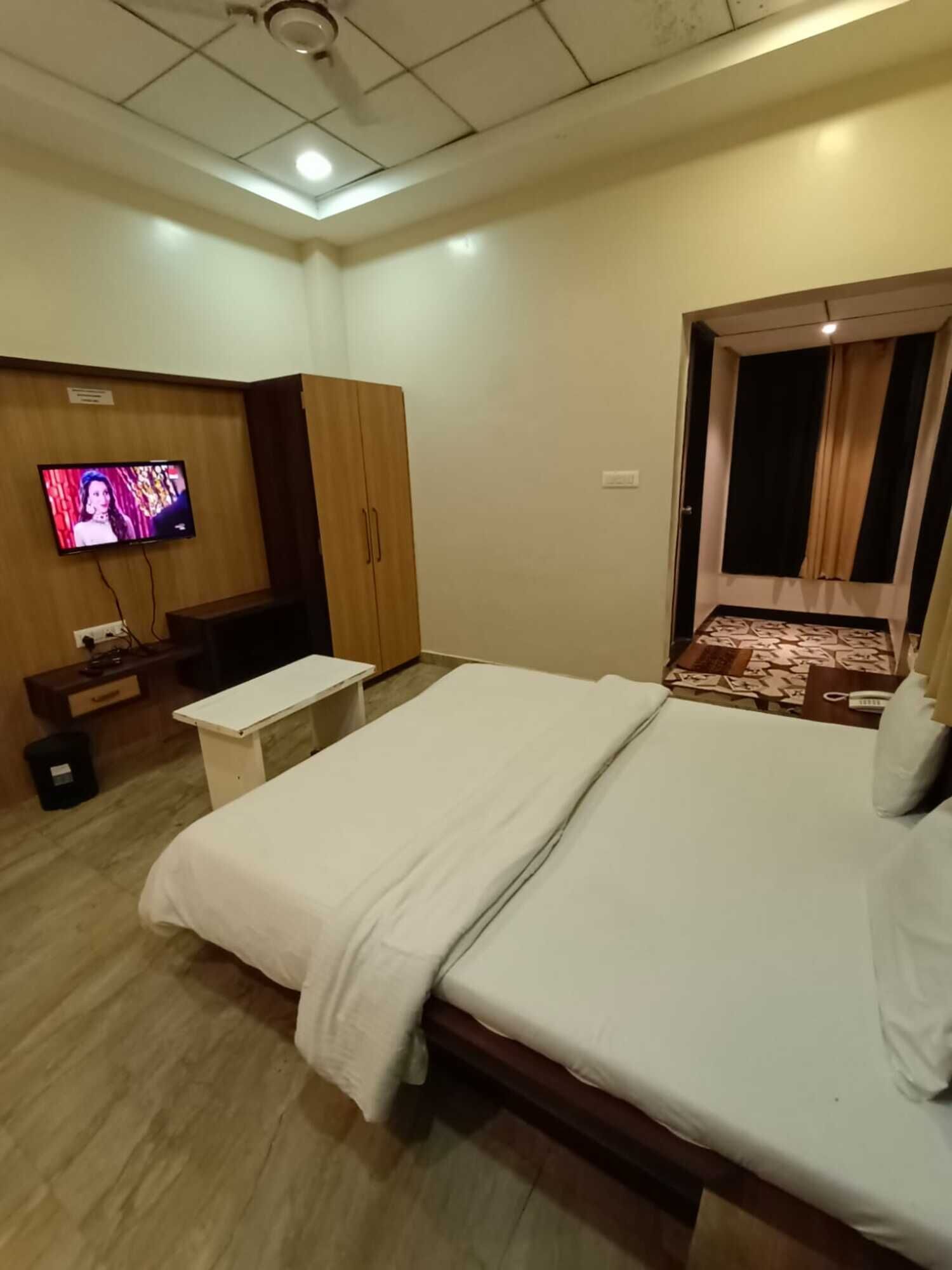 A hotel room with a bed, a TV mounted on the wall, a desk, and a wardrobe.