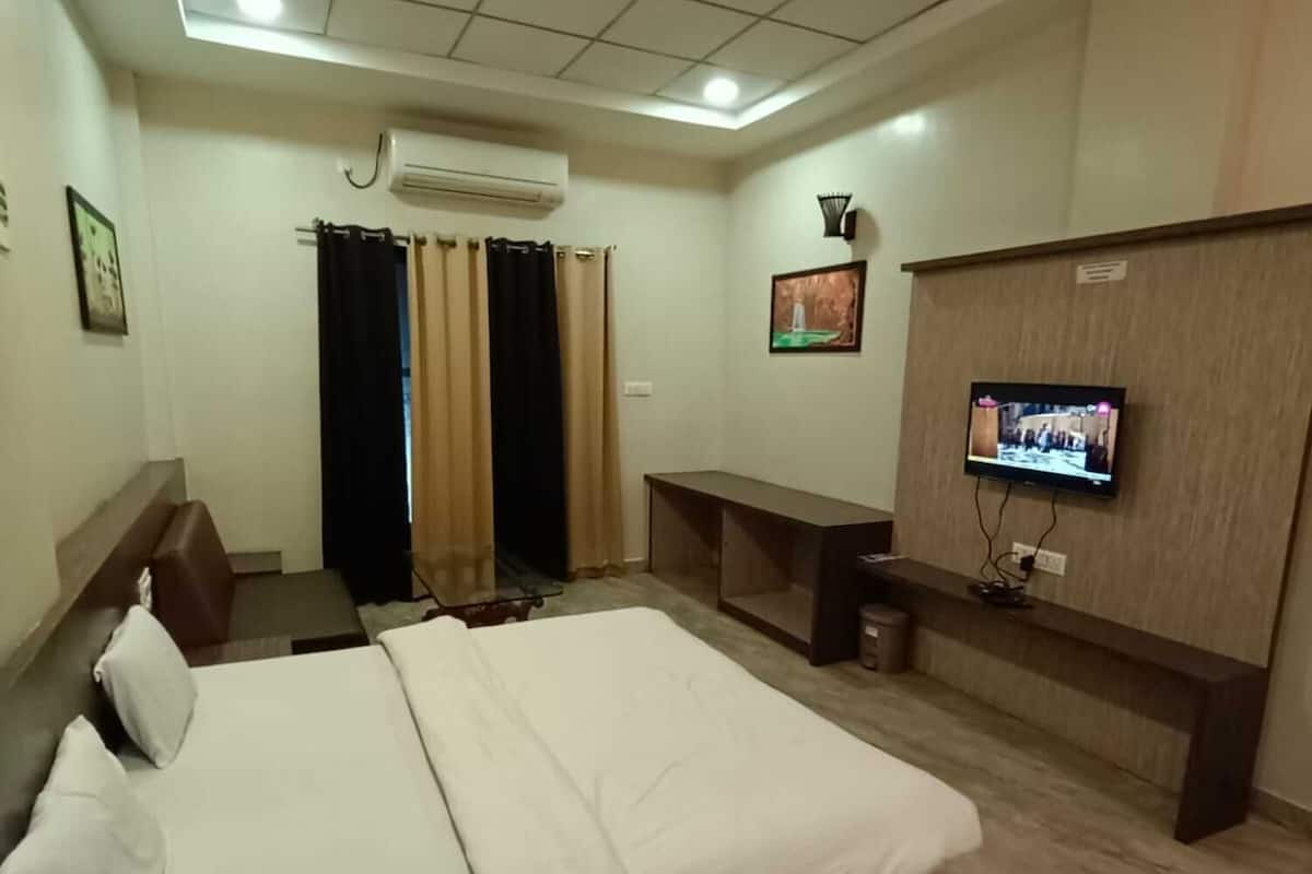 A hotel room with a large bed, a desk, a TV, and an air conditioning unit.