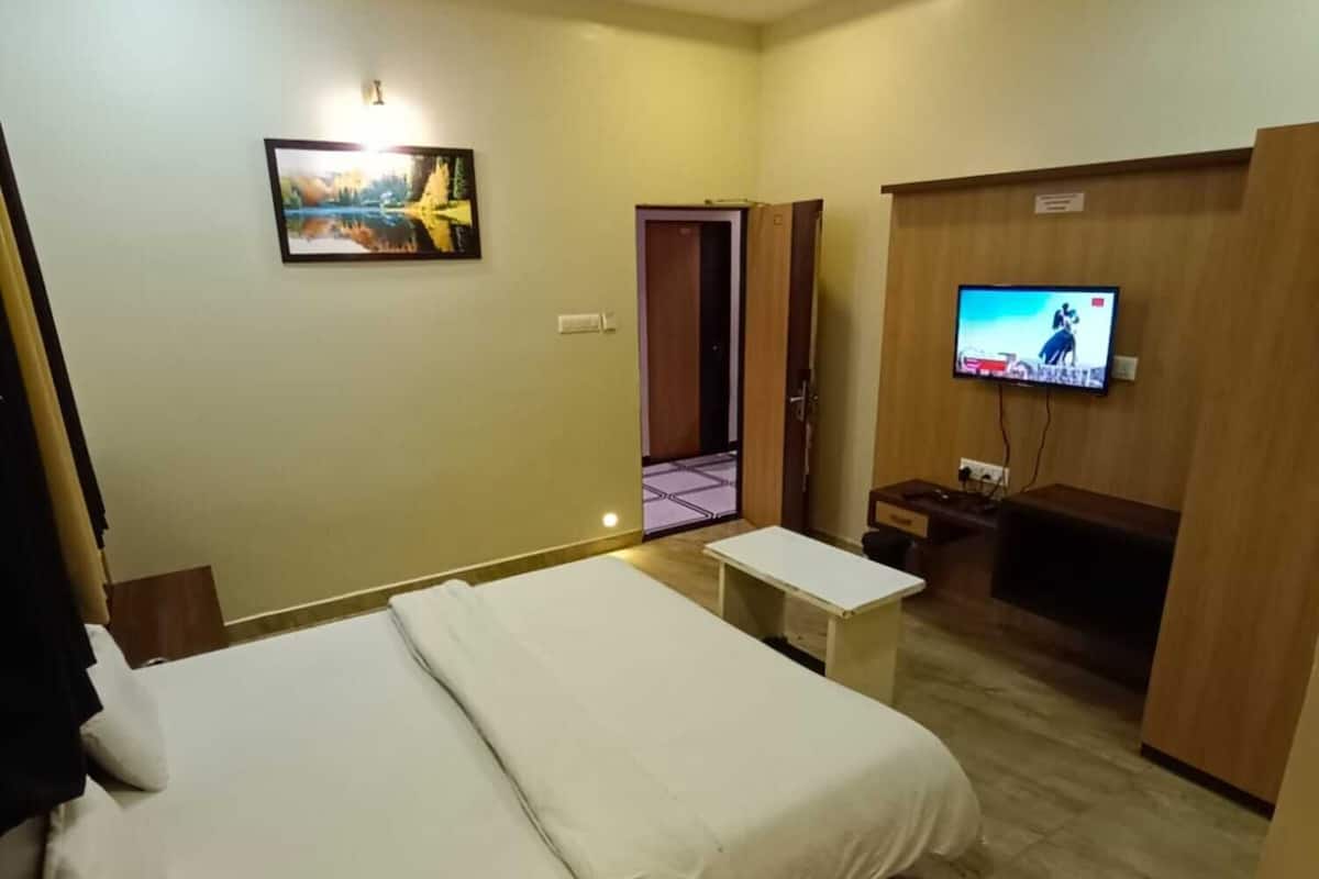 A hotel room with a bed, a small table, a TV, and a painting on the wall.