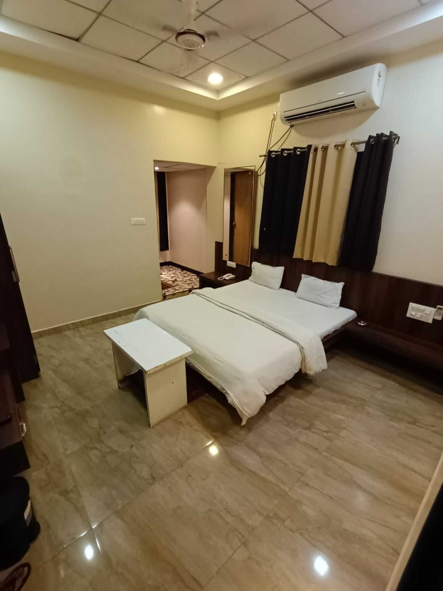 A hotel room with a large bed, a bedside table, a desk, an air conditioning unit, and a mirror.