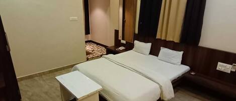 A hotel room with a large bed, a bedside table, a desk, an air conditioning unit, and a mirror.