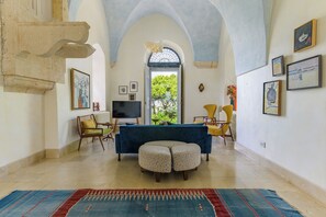 A living room with a sofa, ottoman, and chairs, a television, and artwork on the walls. - Amani Luxury 4BR Villa & Pool in Batroun (Batroun)