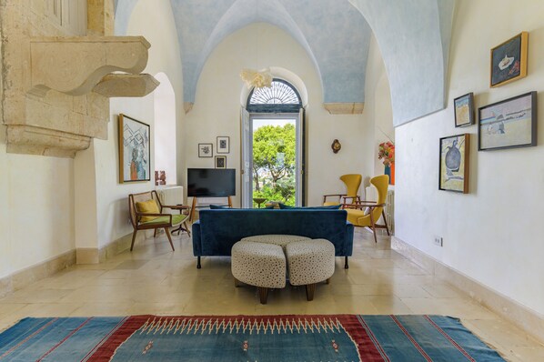 A living room with a sofa, ottoman, and chairs, a television, and artwork on the walls. - Amani Luxury 4BR Villa & Pool in Batroun (Batroun)