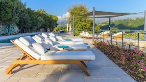 Un espace aménagé au bord de la piscine, avec des chaises longues, un auvent et une vue sur le paysage.