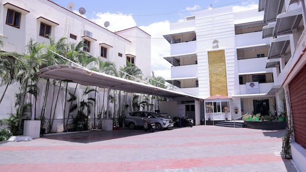 A building with multiple floors, a covered parking area, and a few parked cars. - Shrees Hotel (Perundurai)