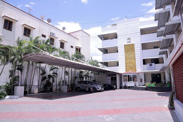A multi-story building with a covered parking area, palm trees, and a car parked inside.