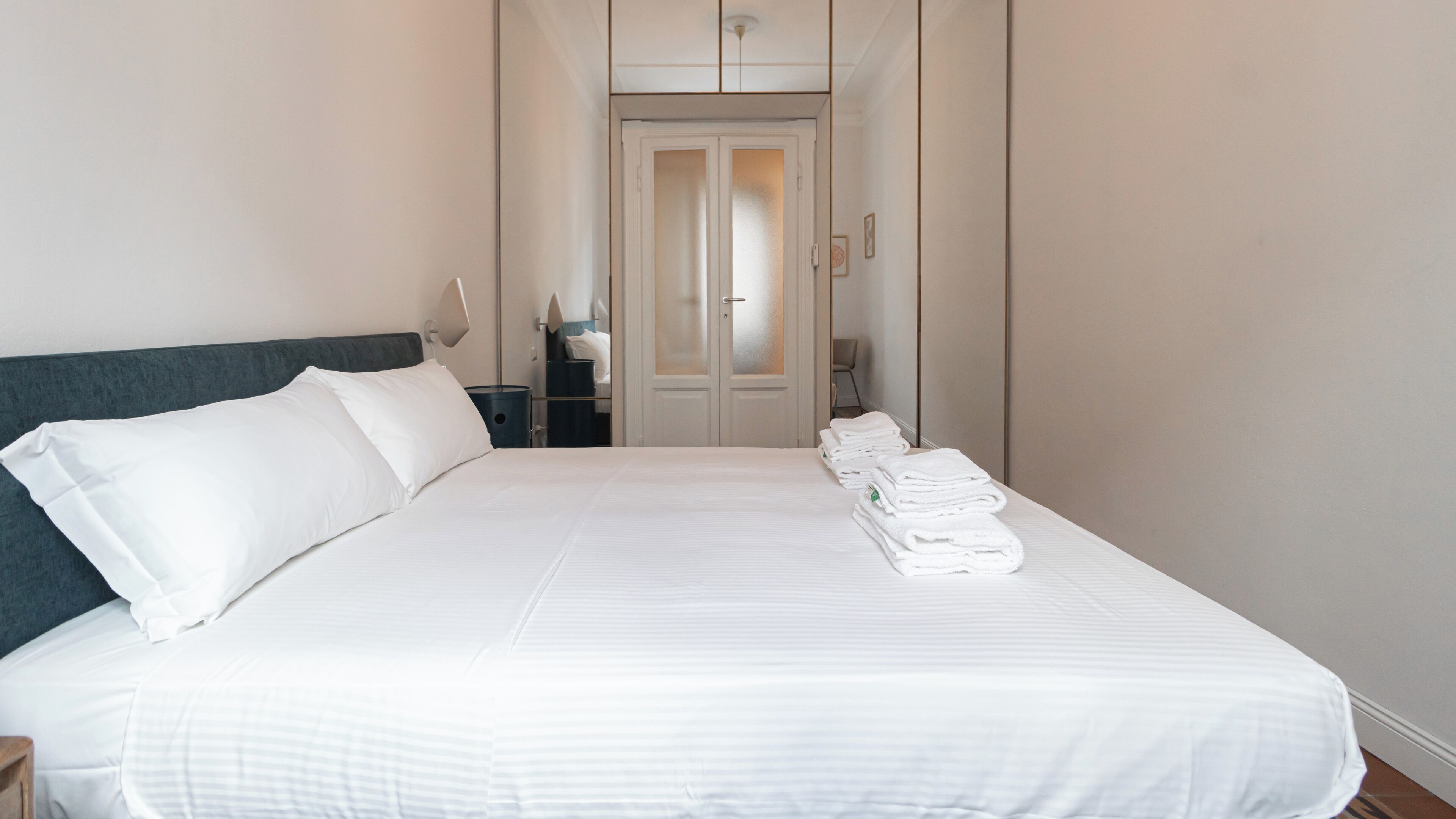 A neatly made bed with white linens, a dark headboard, and a row of folded towels on the foot of the bed.
