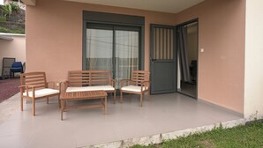 Un espacio exterior techado con sillas de madera y una mesa, una puerta corrediza de vidrio y otra puerta corrediza cerrada.