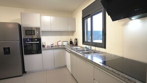 Una cocina moderna con electrodomésticos de acero inoxidable, armarios blancos, encimera de granito y una ventana con marco negro.