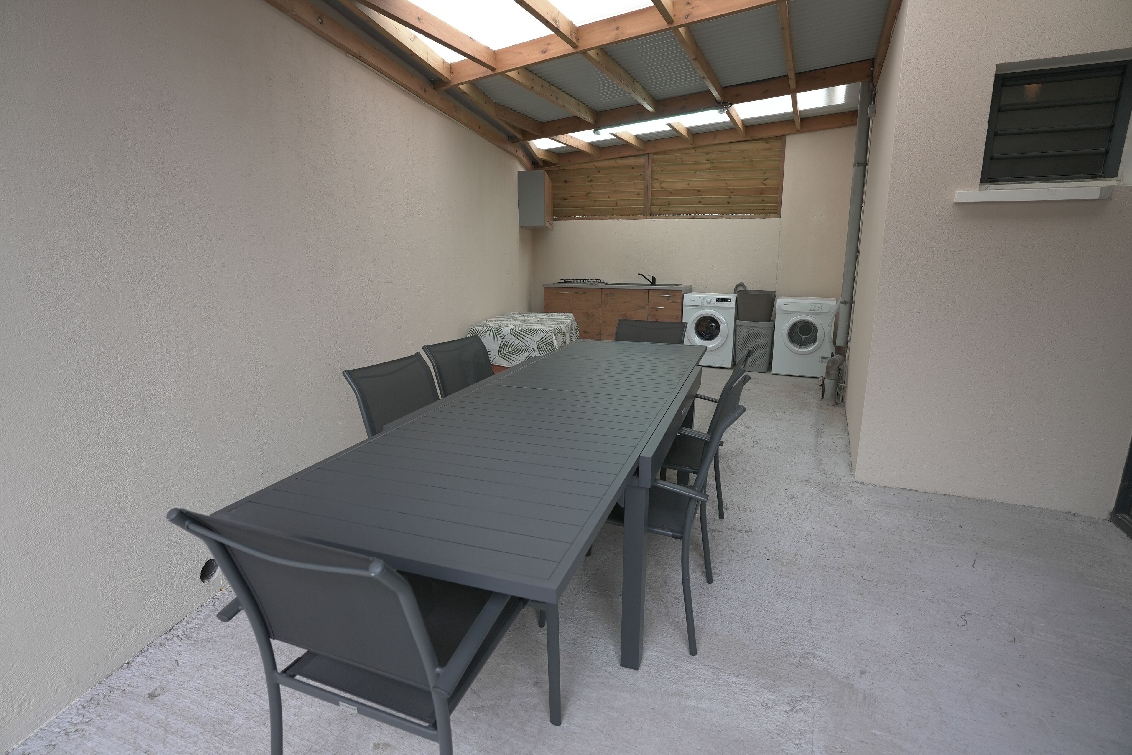 A room with a long table, chairs, a washing machine, and a dryer.