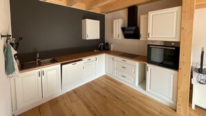 A kitchen with white cabinets, a wooden countertop, a black stove, and a dark wall. - Apartment 'dahoimelig' with mountain view, private terrace and Wi-Fi (Friesenried)