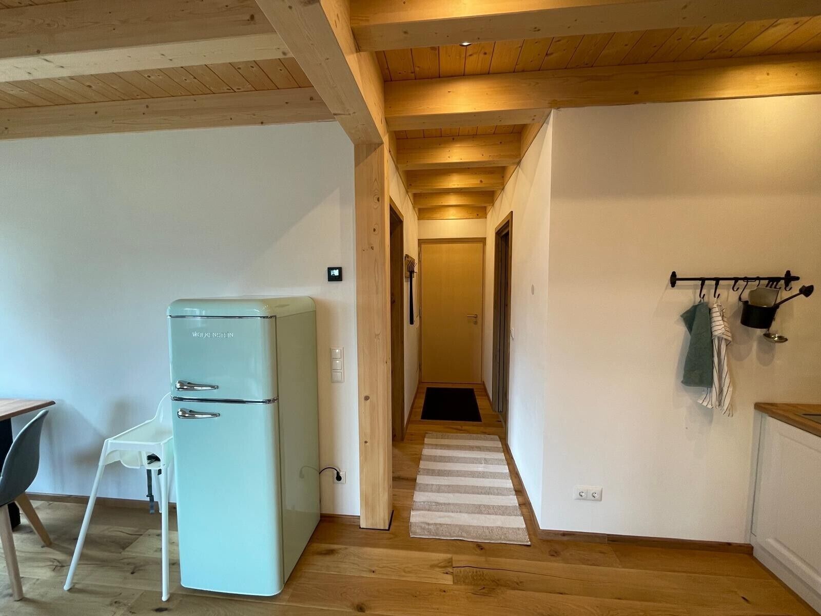 A kitchen with a refrigerator, a dining area with a chair, and a hallway leading to another room.