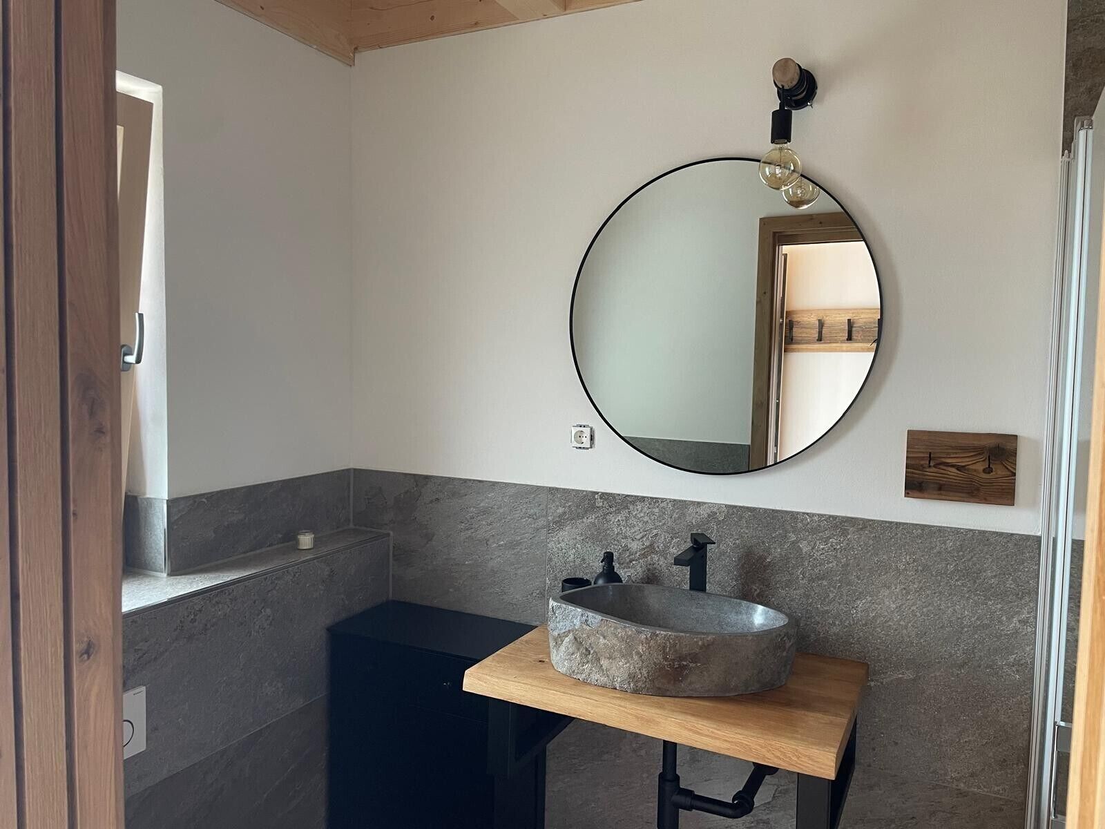 Een badkamer met een ronde spiegel, een stenen wastafel en een houten wastafelmeubel.