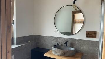 Een badkamer met een ronde spiegel, een stenen wastafel en een houten wastafelmeubel.