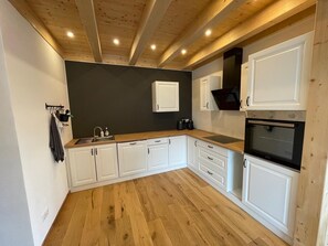 Eine Küche mit weißen Schränken, einer Holz Arbeitsplatte, einem eingebauten Ofen und einer dunklen Wand.