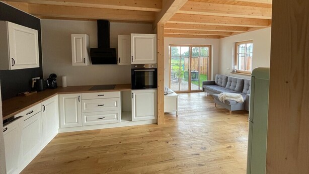 A spacious kitchen with wooden cabinets, a black stove, and a large sliding glass door leading to an outdoor area. - Apartment 'dahoimelig' with mountain view, private terrace and Wi-Fi (Friesenried)