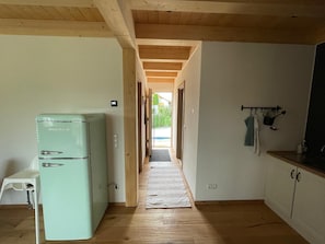 A kitchen with a vintage refrigerator, wooden flooring, and a view through an open door.