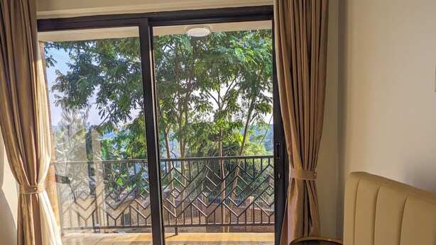 Une chambre d’hôtel avec un grand lit, une vue sur un balcon doté d’une balustrade et des rideaux aux fenêtres.