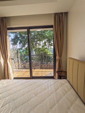 Habitación de hotel con una cama grande, vistas a un balcón con barandilla y cortinas en las ventanas.