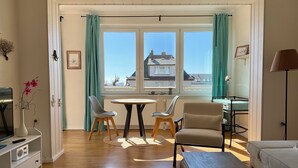 A living room with a sofa, a table, two chairs, a lamp, a radiator, and a window with curtains.
