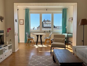 A living room with a sofa, a table, two chairs, a lamp, a radiator, and a window with curtains.
